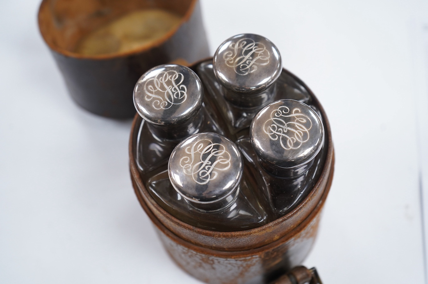 A cased set of four Edwardian silver mounted glass travelling scent bottles, with engraved monogram, George Bedingham, London, 1901, housed in a circular leather carrying case, bottles 14.5cm. Condition - fair to good an